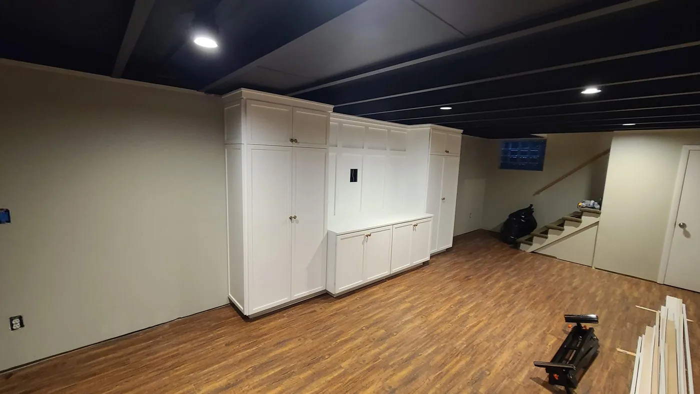 Finished basement with a dark painted ceiling, white built in cabinetry and wood look flooring
