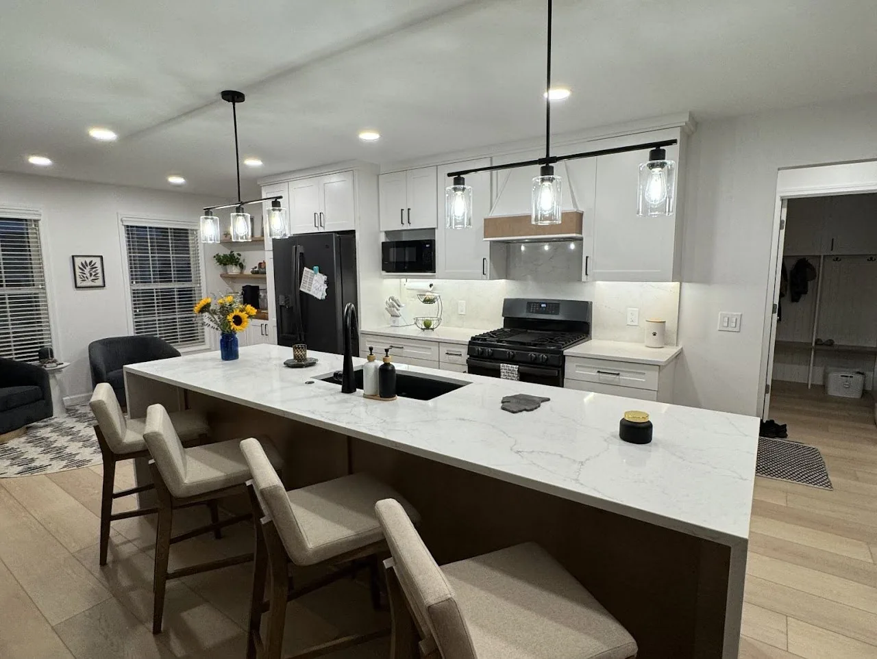 Kitchen remodeled by We Love to Remodel, with a long quartz island, four stools and black pendant lights