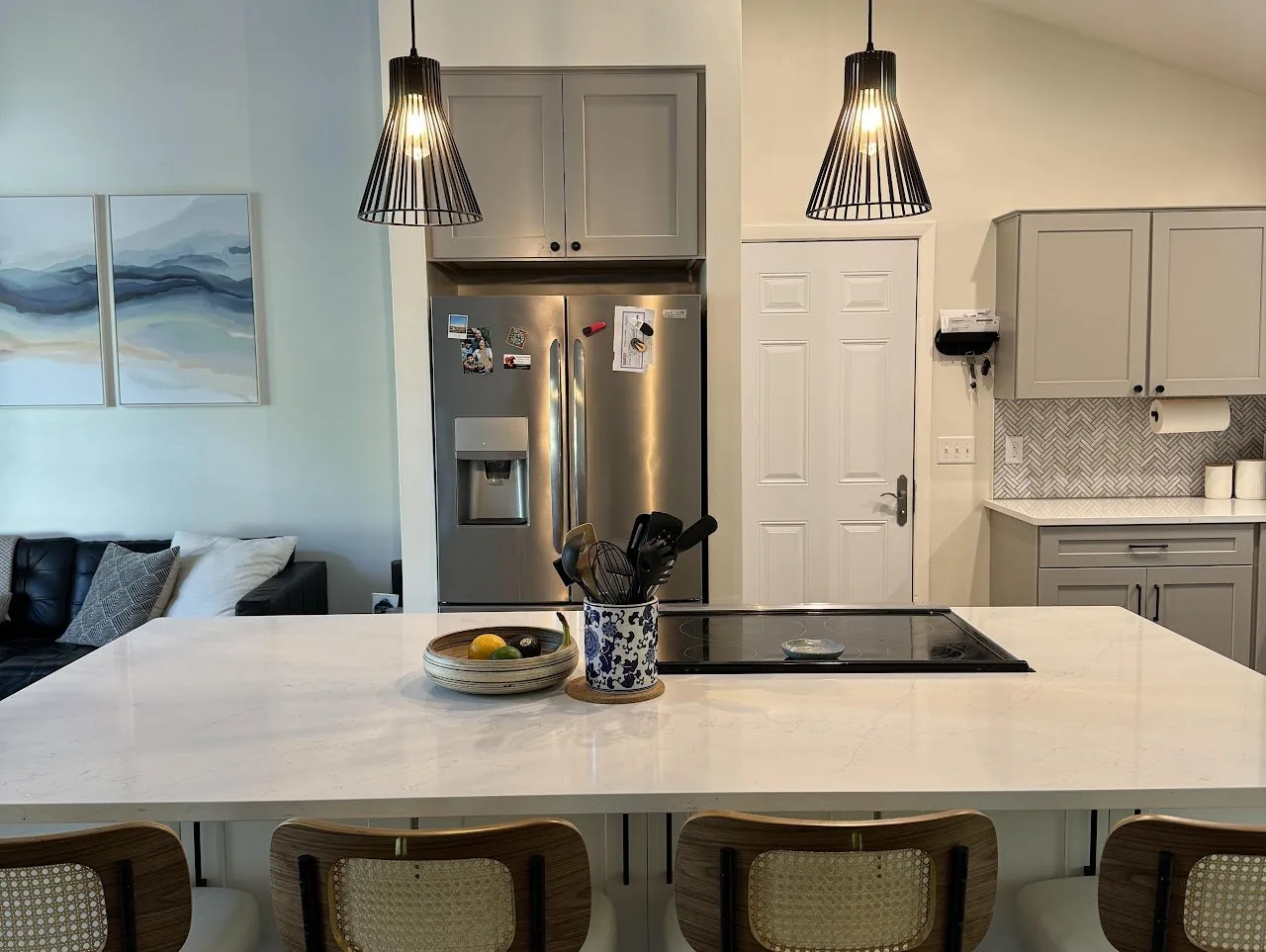 Kitchen island with an induction cooktop, cane back stools and black pendant lights