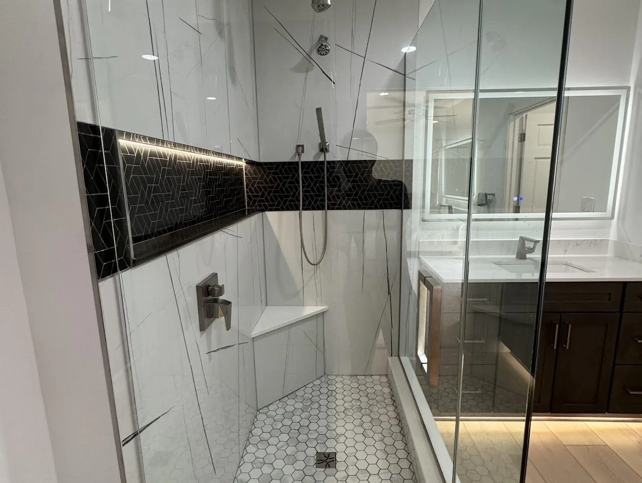 Walk in glass shower with a dark mosaic accent band and hexagon floor tile